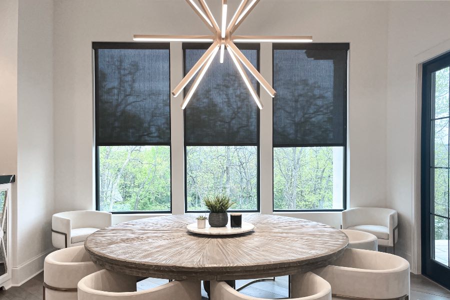 Black motorized shades on three windows in a beige dining room